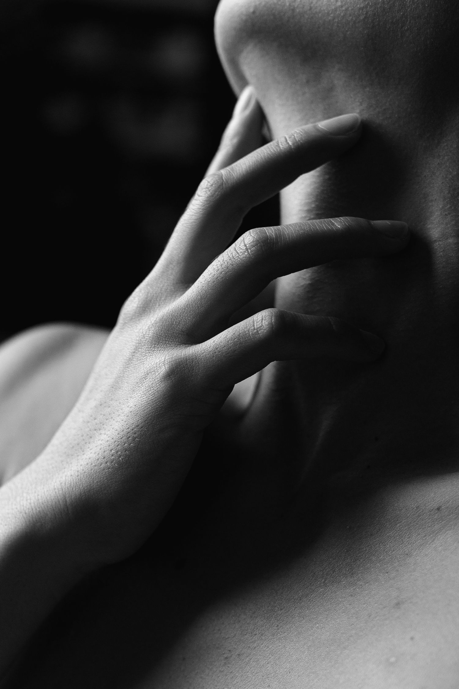 Black and white close-up of a hand gently touching a persons neck, artistic fine art photography.