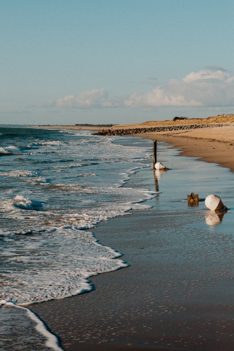 Les vagues caressent doucement une plage de sable fin, bordée de poteaux et de bouées en bois, à l'heure dorée à Saint Martin de Bréhal.