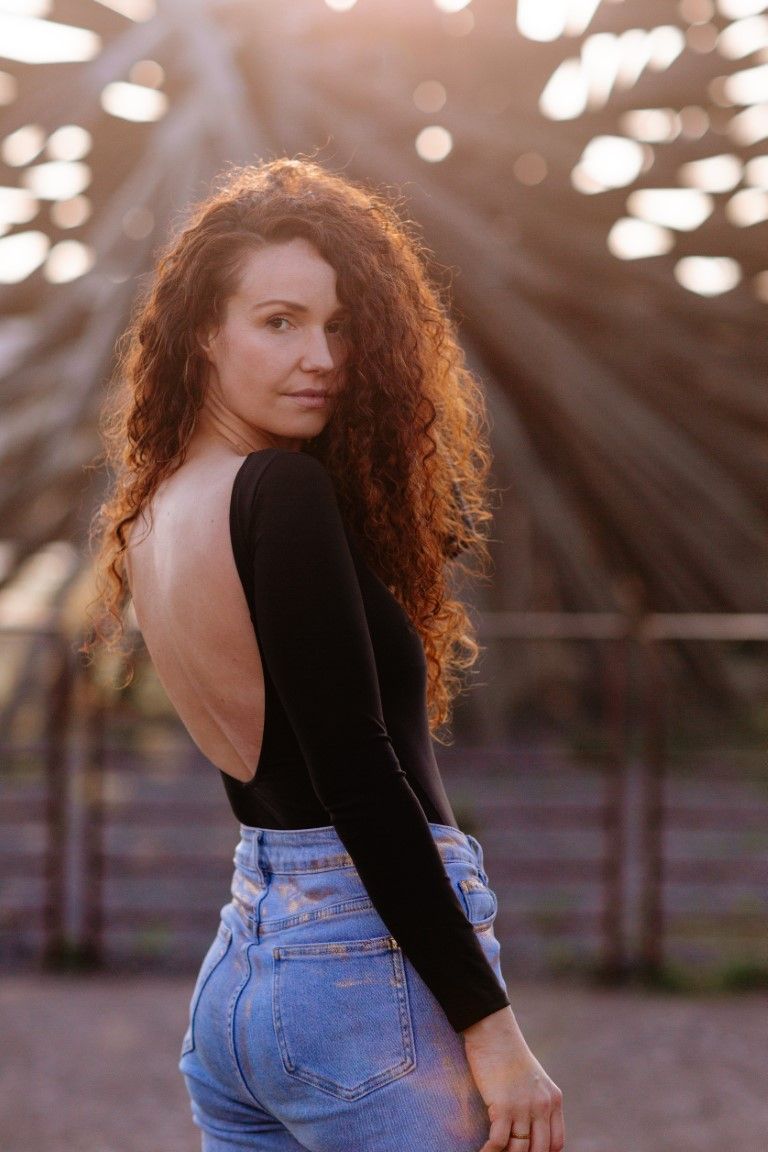 Femme rousse en body noir dos nu et jean, posant en extérieur sous la lumière dorée du soleil à Nantes