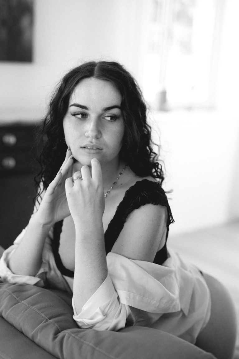 Portrait en noir et blanc d'une femme aux cheveux bouclés, portant un soutien-gorge en dentelle noire, le menton appuyé sur sa main.