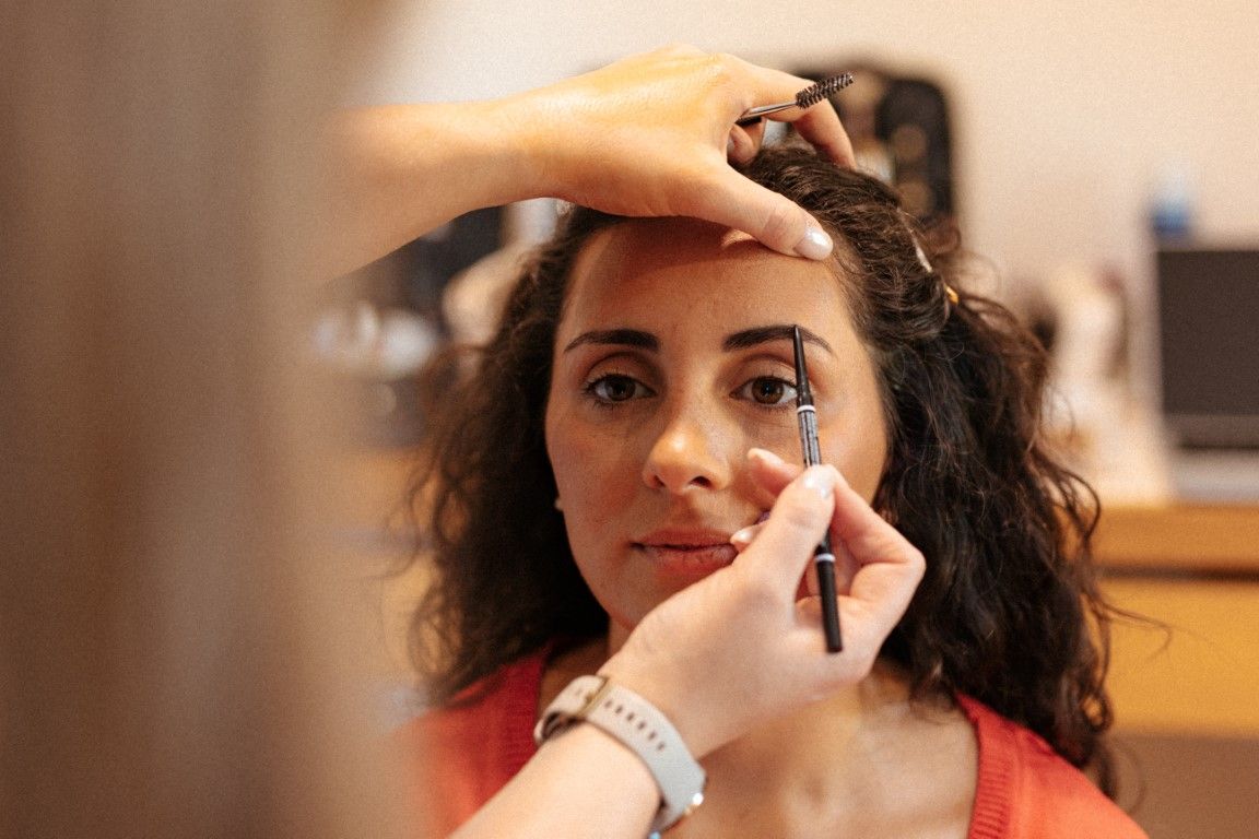 Woman having eye makeup applied by a makeup artist using brushes and pencils in a bright studio setting.