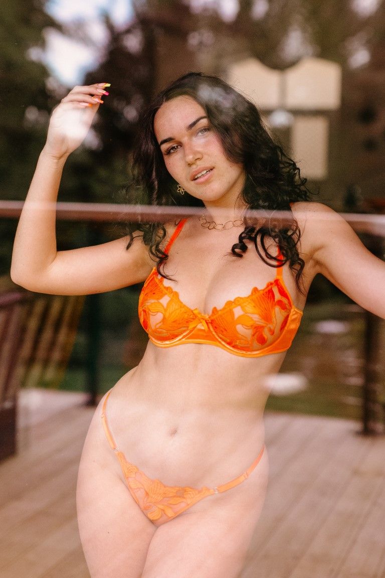 Woman in orange floral lace lingerie set on balcony.