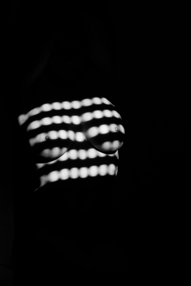 Torse nu artistique en noir et blanc avec un motif clair rayé sur fond sombre.