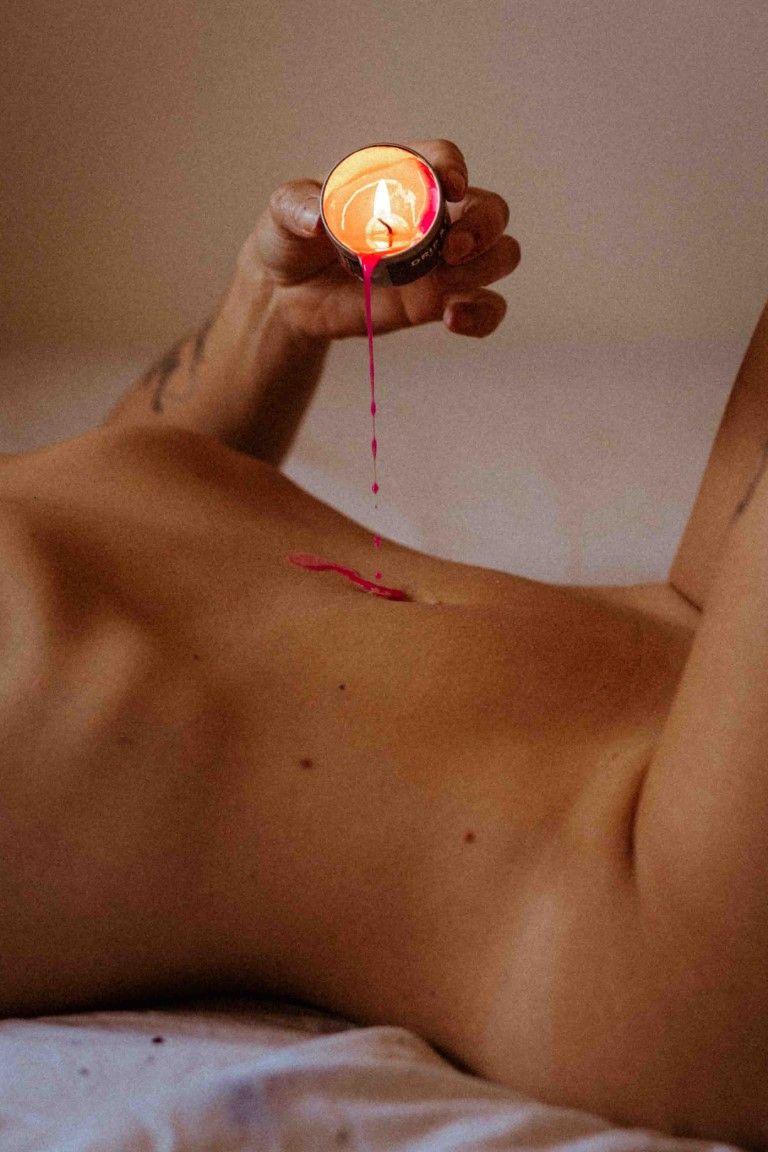 Artistic boudoir photo of candle wax dripping onto bare skin in warm candlelight.