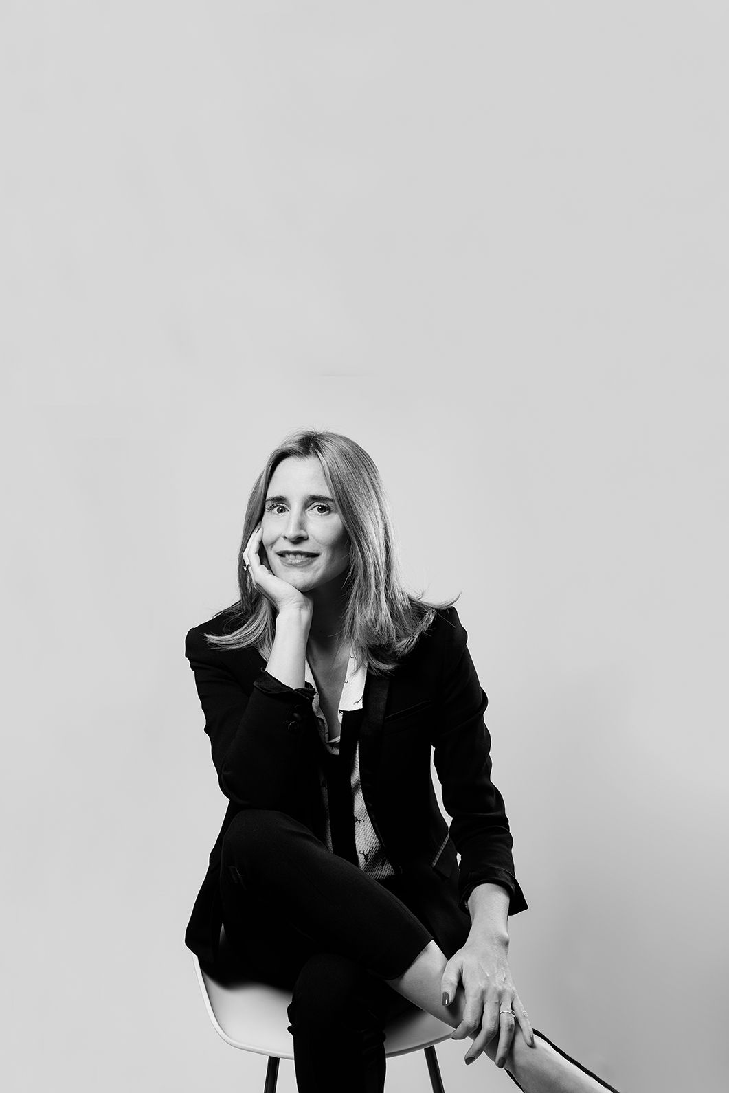Elegant woman in black blazer sitting on chair in thoughtful pose in studio portrait.