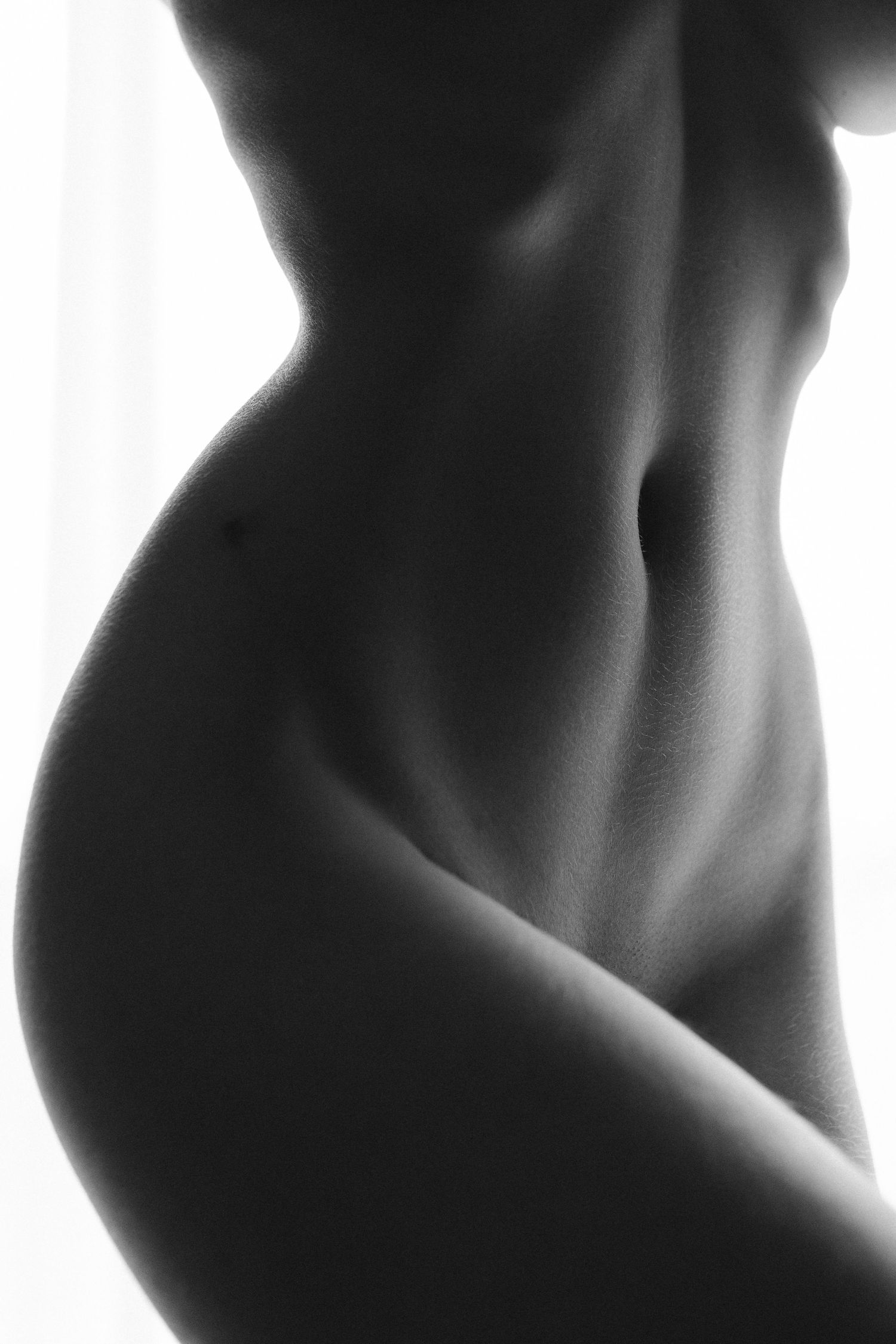 Photographie artistique de nu en noir et blanc mettant en valeur les courbes féminines et la silhouette tonique du torse sur fond de douce