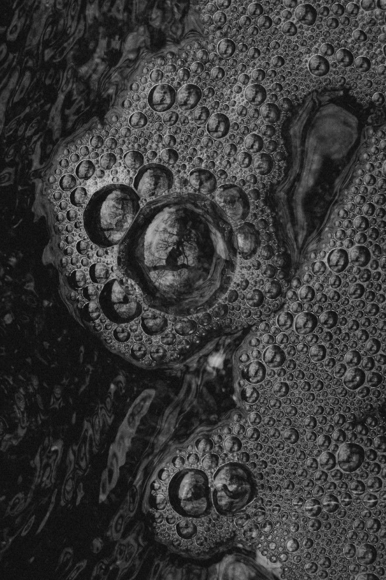 Macrophotographie en noir et blanc de gouttelettes d'eau sur une surface texturée à motifs circulaires.