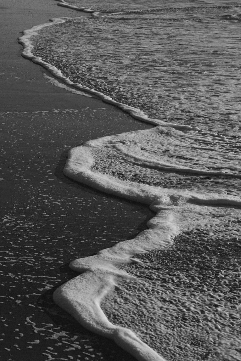 Photographie en noir et blanc de douces vagues océaniques sur une plage de sable fin en Normandie.