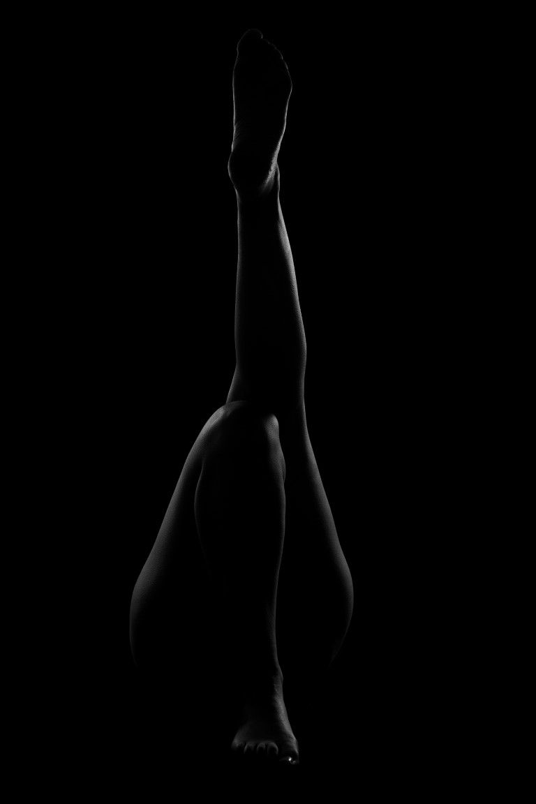 Black and white artistic silhouette of a woman's legs raised upward against a dark background.
