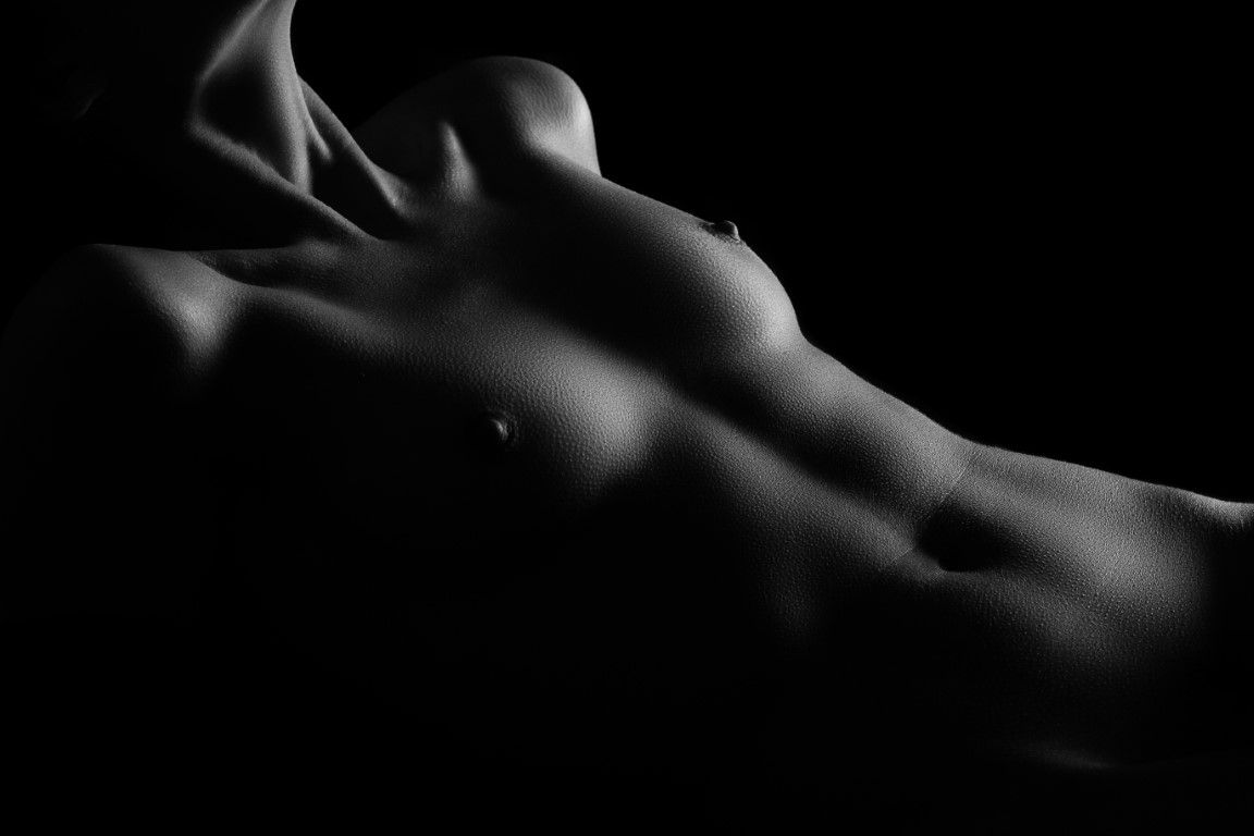 Black and white fine art nude photography showcasing dramatic light and shadow on a reclining female torso.