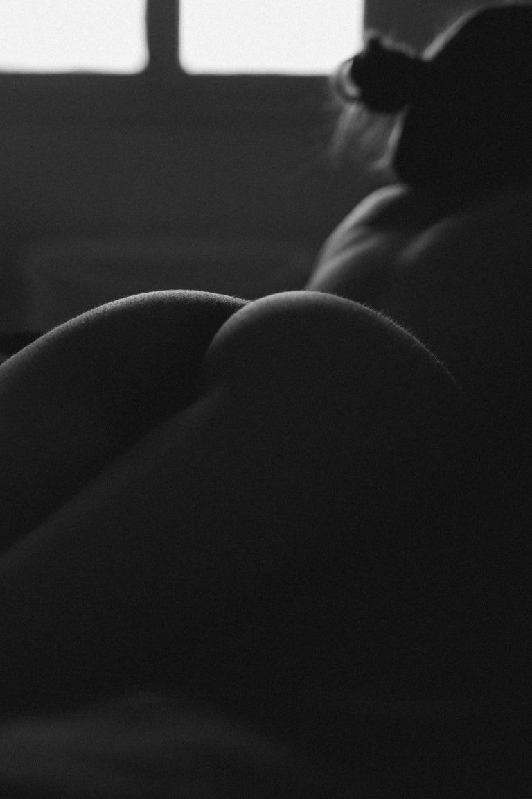 Photographie artistique en noir et blanc d'un nu mettant en valeur les douces courbes du corps d'une femme dans une lumière tamisée.