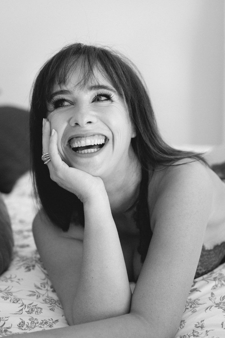 Black and white portrait of laughing brunette woman lying on bed resting chin on hand.