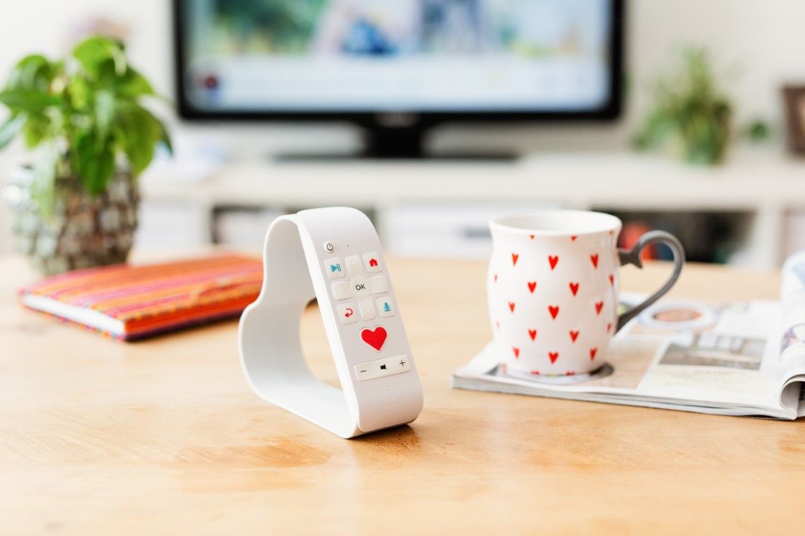 White heart-shaped smart home device on wooden desk beside a red heart-print mug.