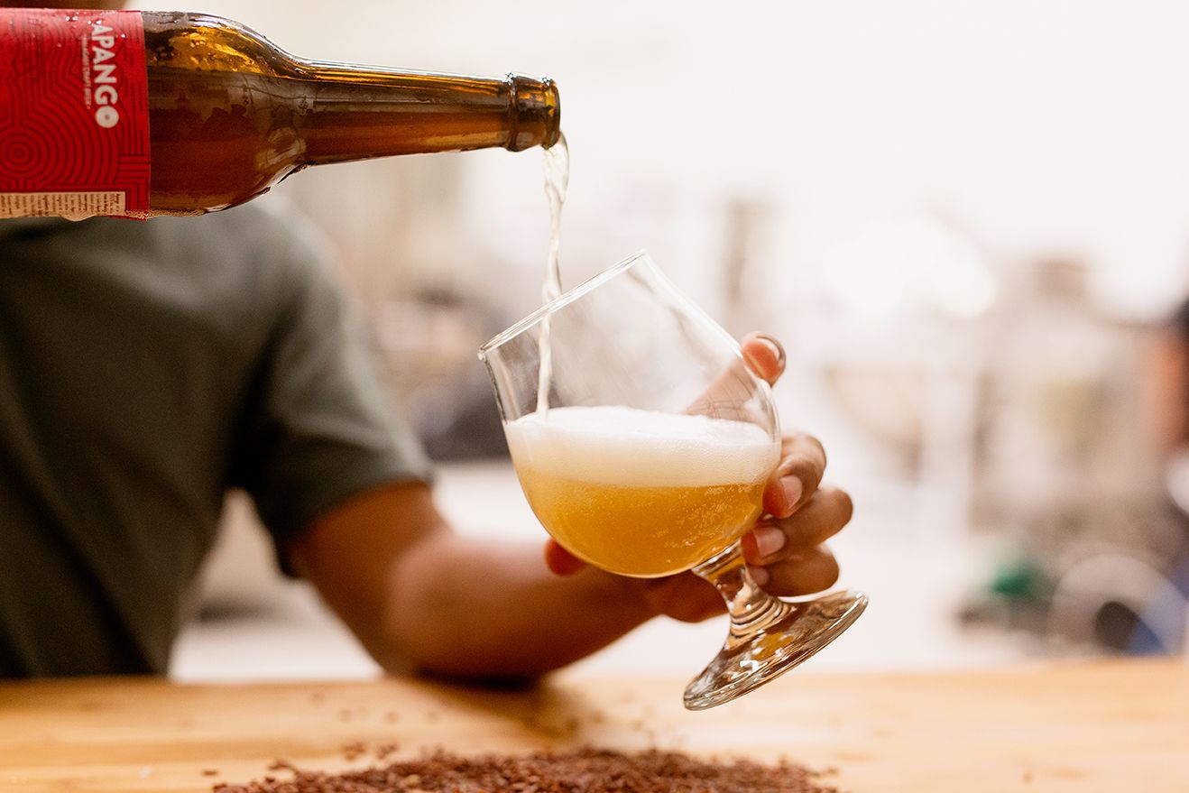 Beer being poured from an Apango bottle into a tulip glass with a frothy head.