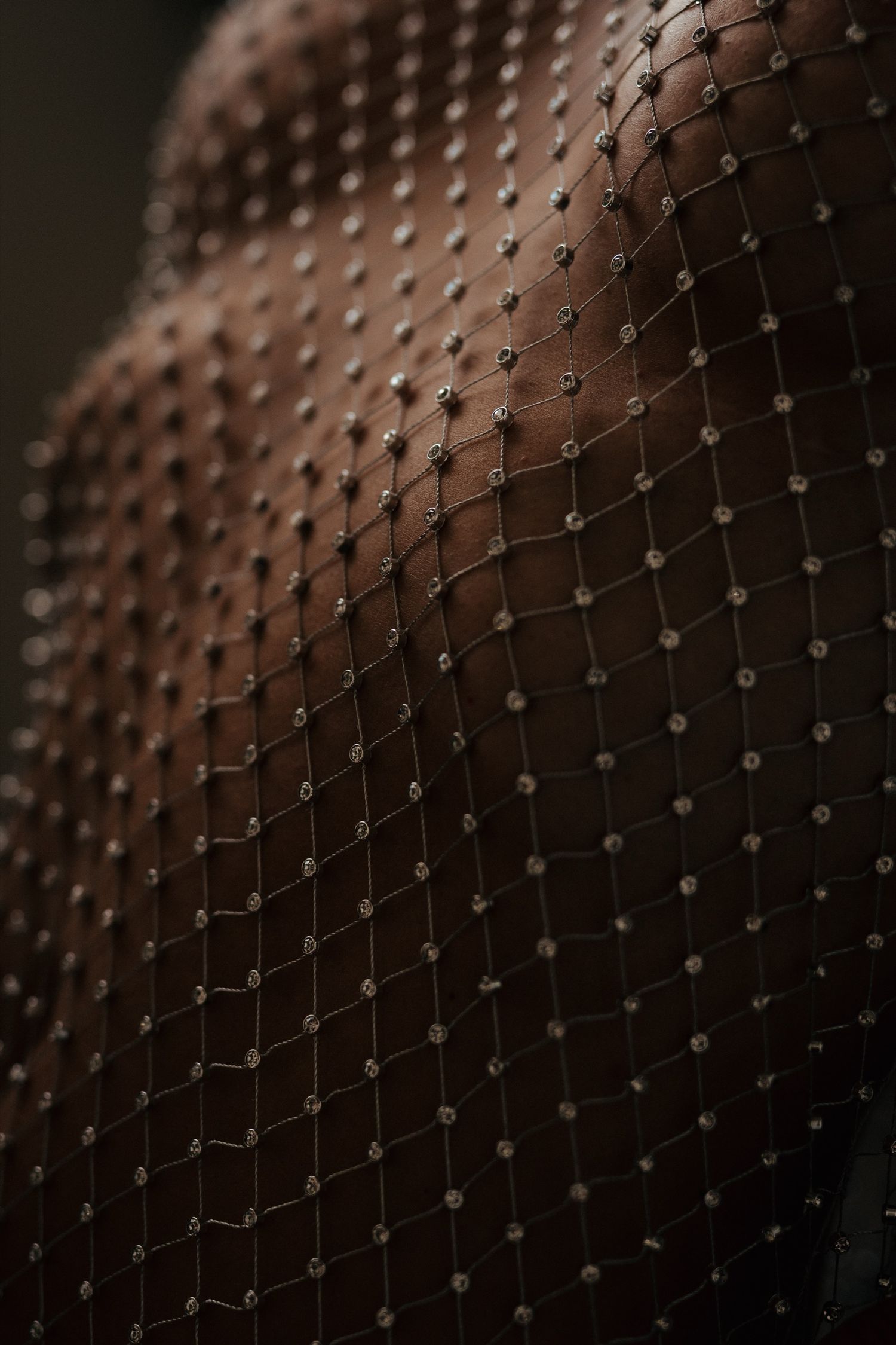 Close-up of sheer black fishnet fabric adorned with small rhinestone embellishments, creating an elegant diamond pattern.