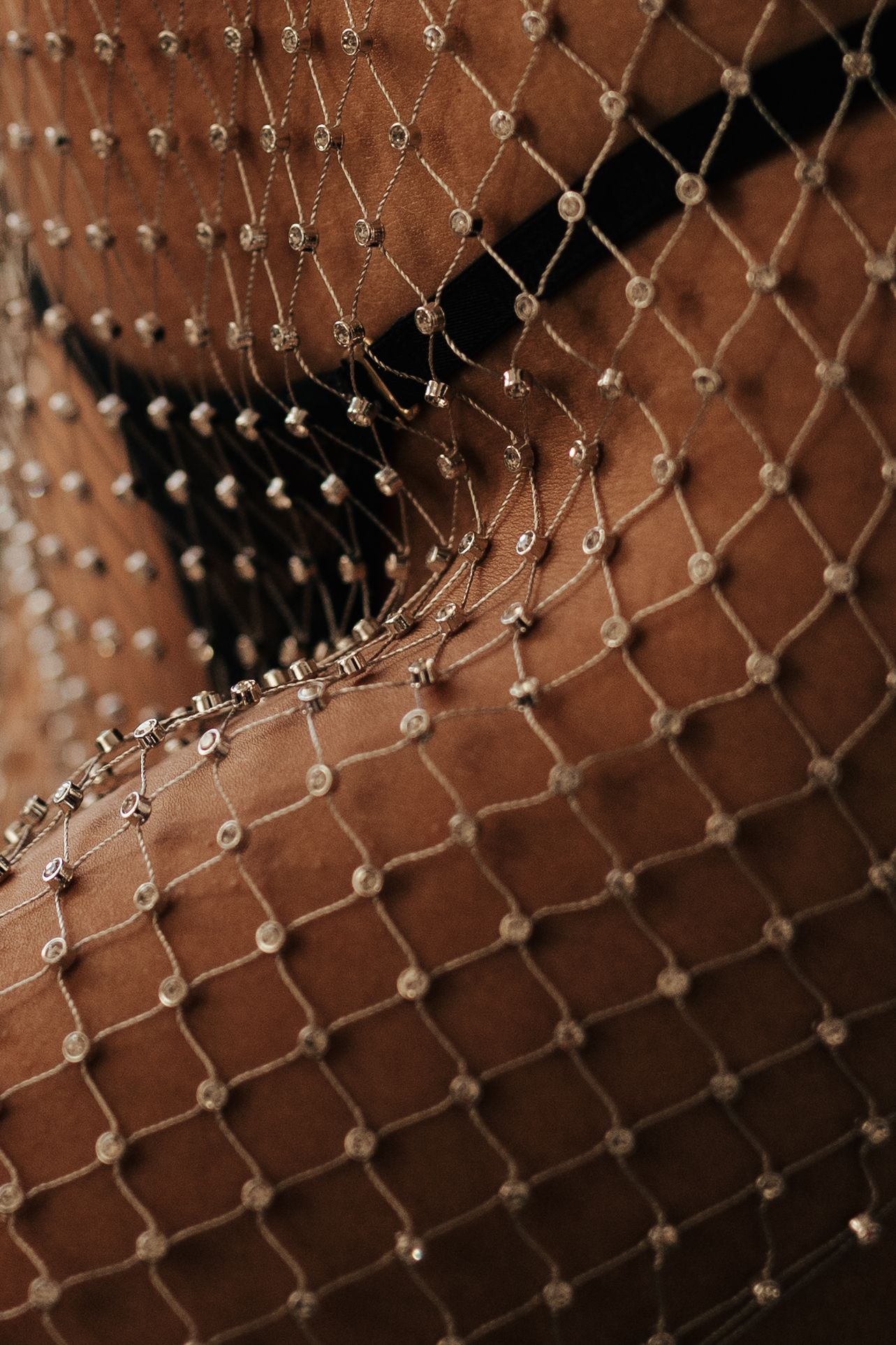 Close-up of elegant beaded net veil with crystal embellishments draped over warm brown fabric.