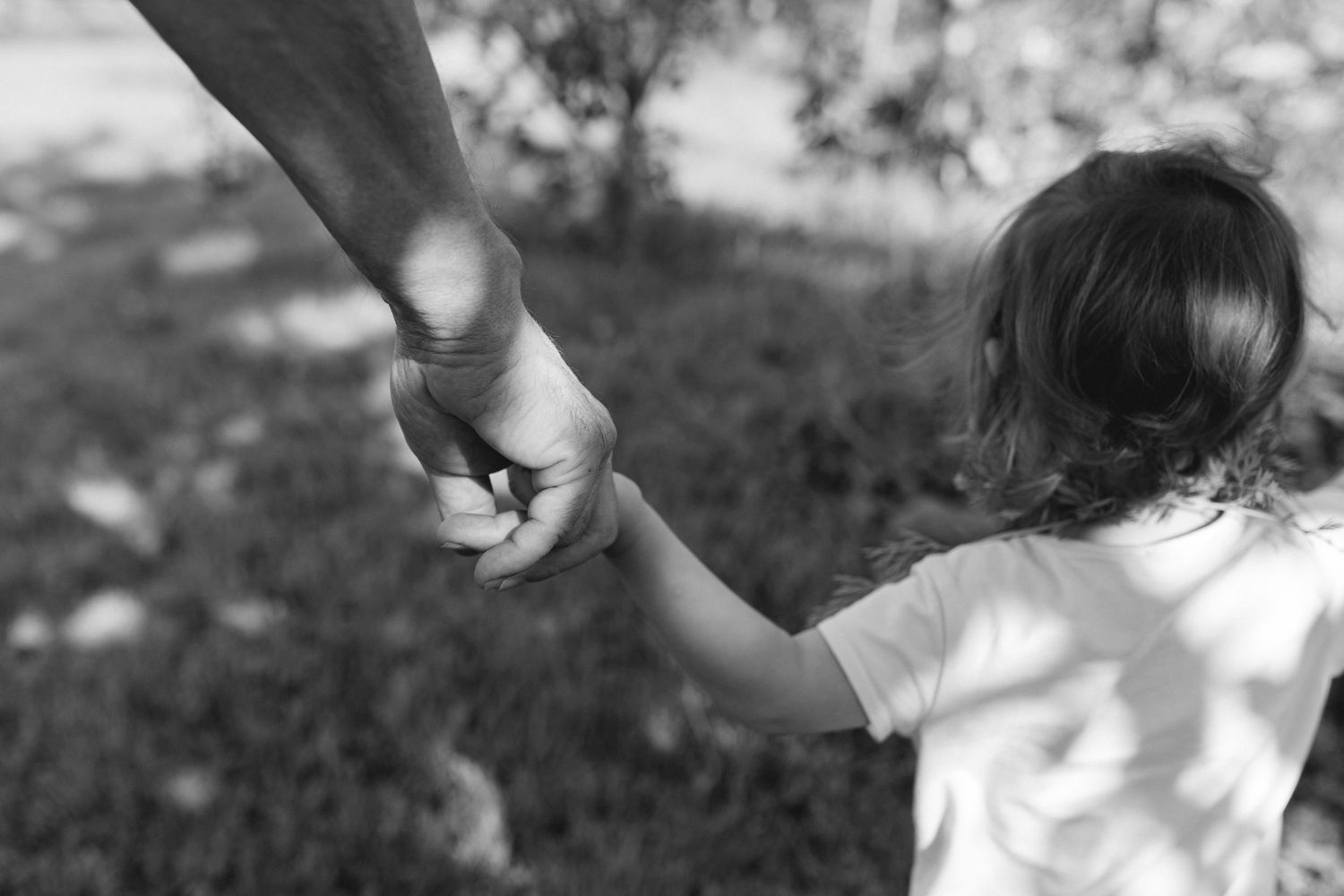 Photo en noir et blanc d'un adulte tenant la main d'un jeune enfant à l'extérieur.