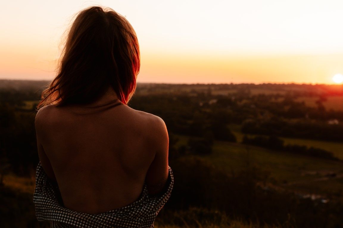 Femme au dos nu contemplant un coucher de soleil pittoresque sur la campagne depuis le sommet d'une colline
