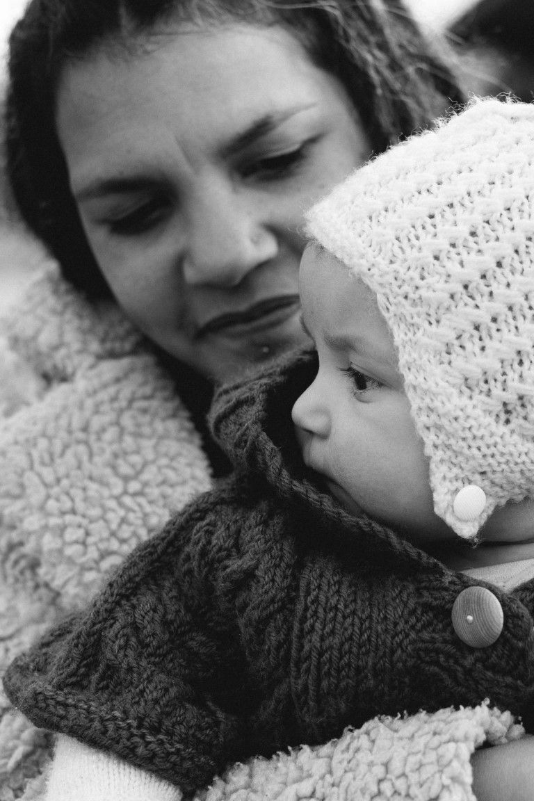 Photo en noir et blanc d'une mère tenant tendrement son nouveau-né vêtu d'un bonnet et d'une tenue tricotés.
