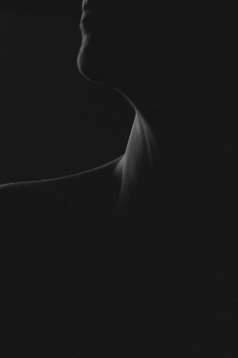 Silhouette minimaliste en noir et blanc du cou et de la clavicule d'une femme sur fond sombre.