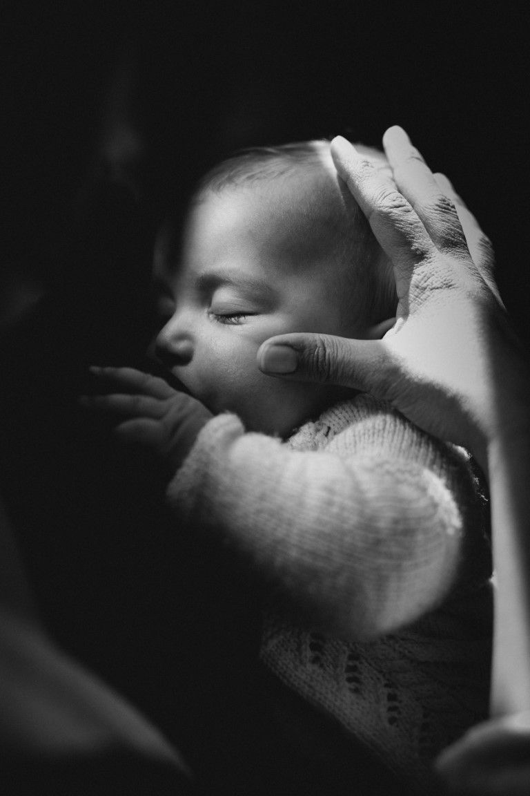Photo en noir et blanc d'un nouveau-né endormi, doucement bercé dans les mains d'un adulte lors de l'allaitement.
