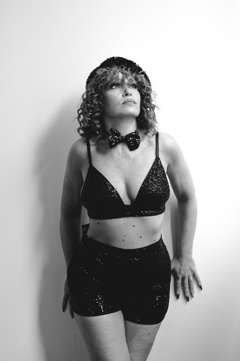 Woman in black sequin bralette, shorts, and bow tie poses dramatically in black and white photo.