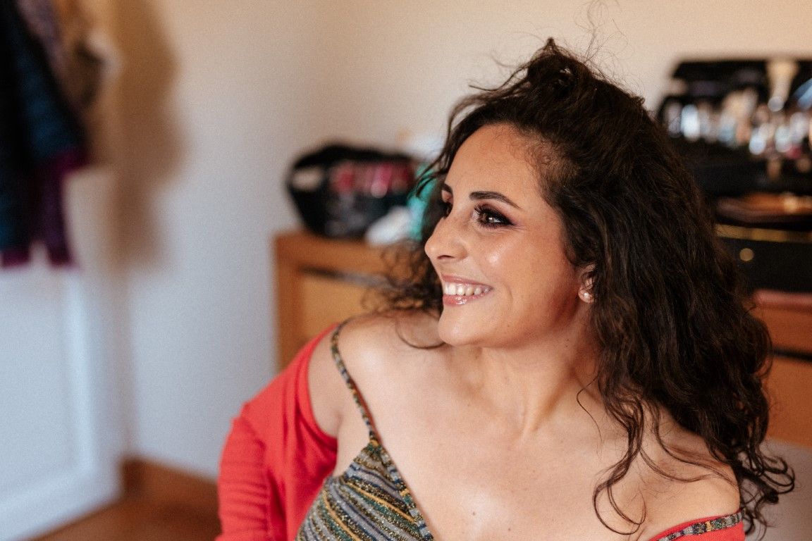 Smiling brunette woman in red cardigan and striped top, looking sideways in a bright room.