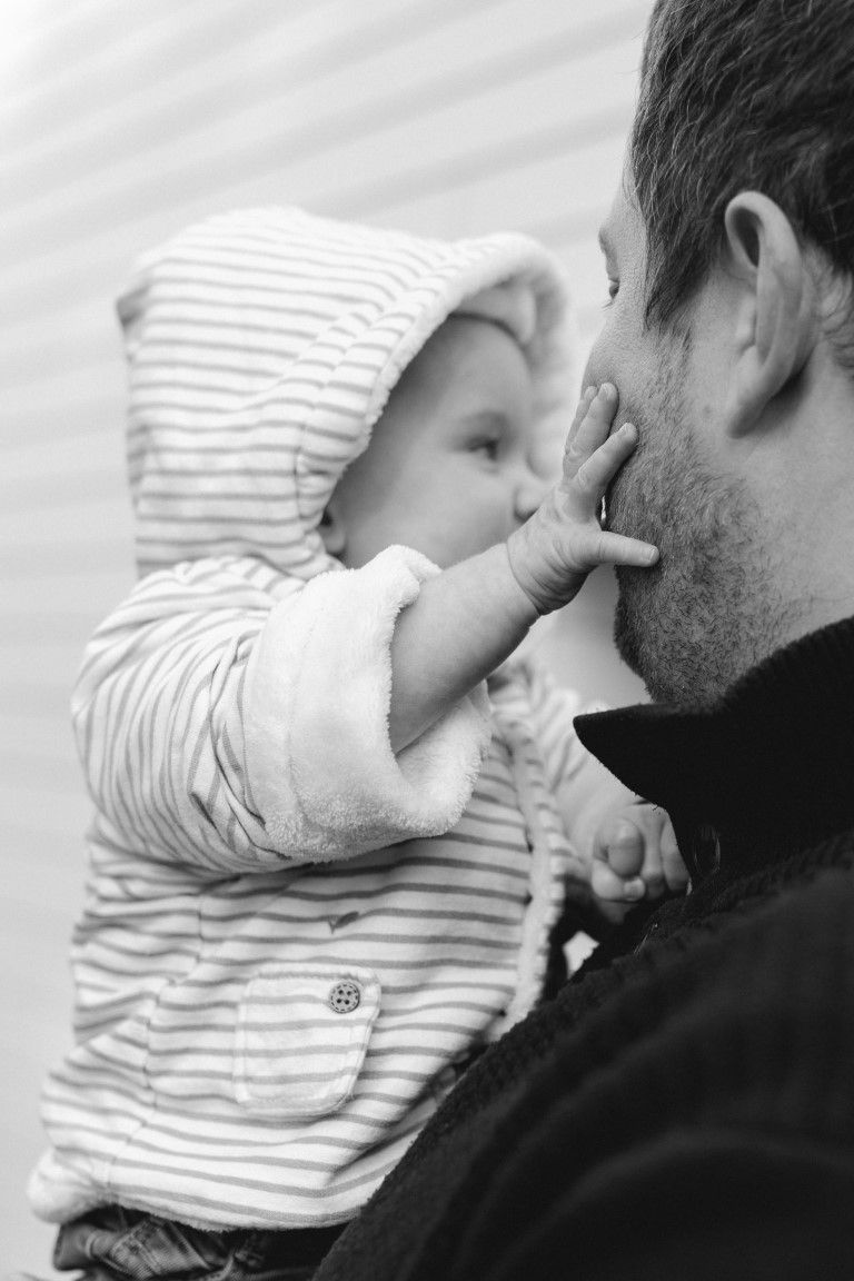 Photo en noir et blanc d'un bébé portant un sweat-shirt à rayures touchant le visage de son père.