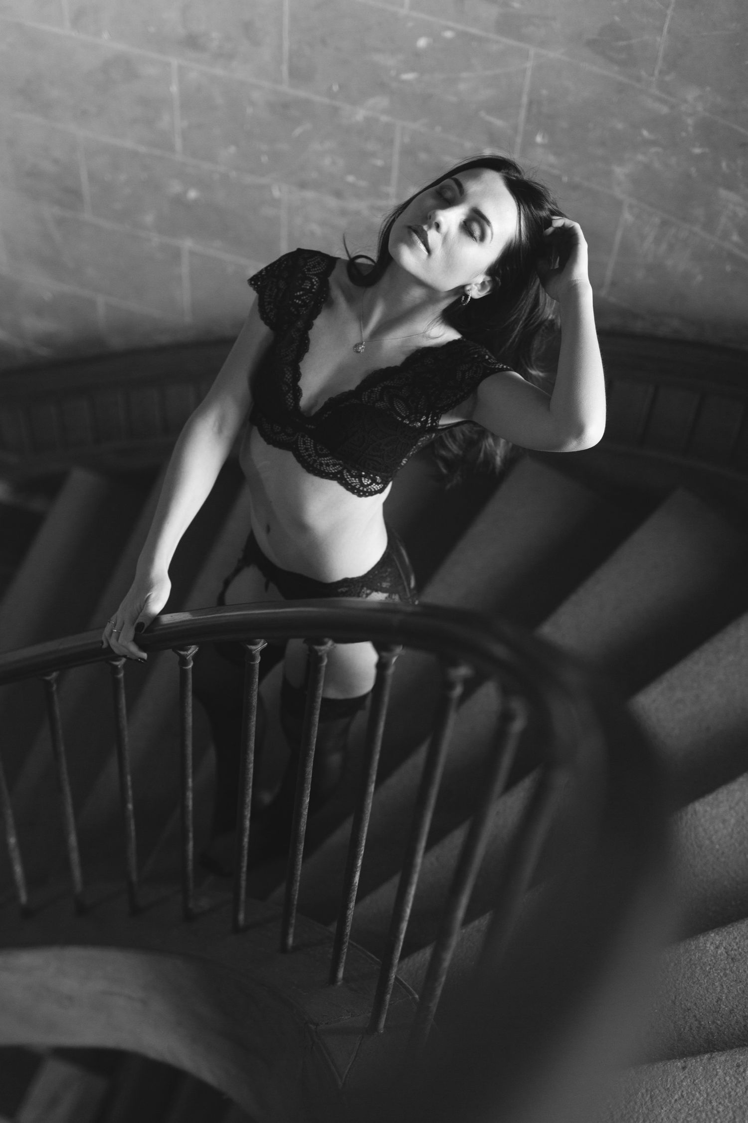 Black and white photo of a woman in lace lingerie posing gracefully on a spiral staircase.