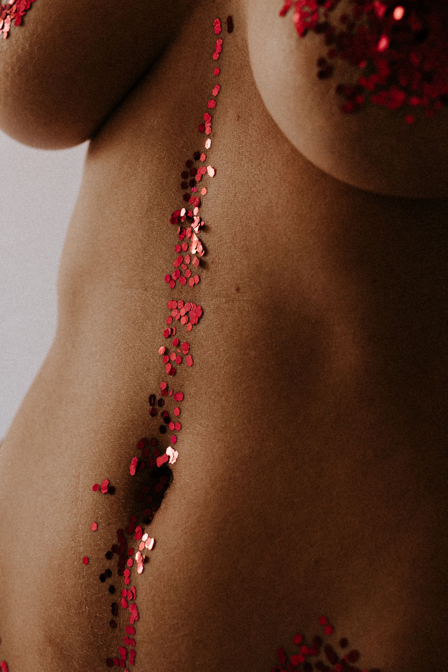Close-up of a torso adorned with red and pink glitter sequins arranged in a vertical line on skin.
