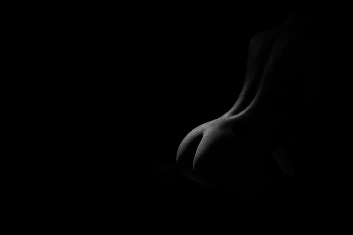 Black and white artistic nude silhouette highlighting curves against dark background.
