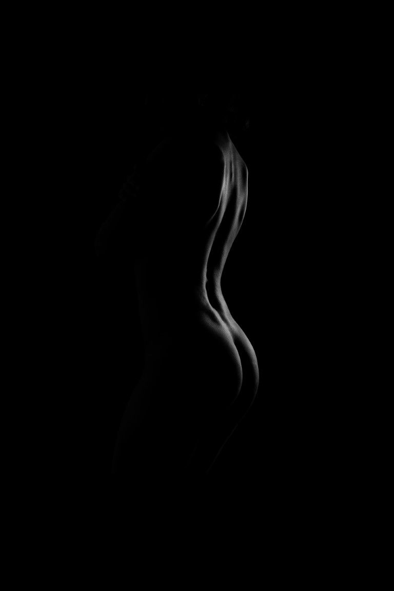 Black and white silhouette of a womans curved body against dark background.