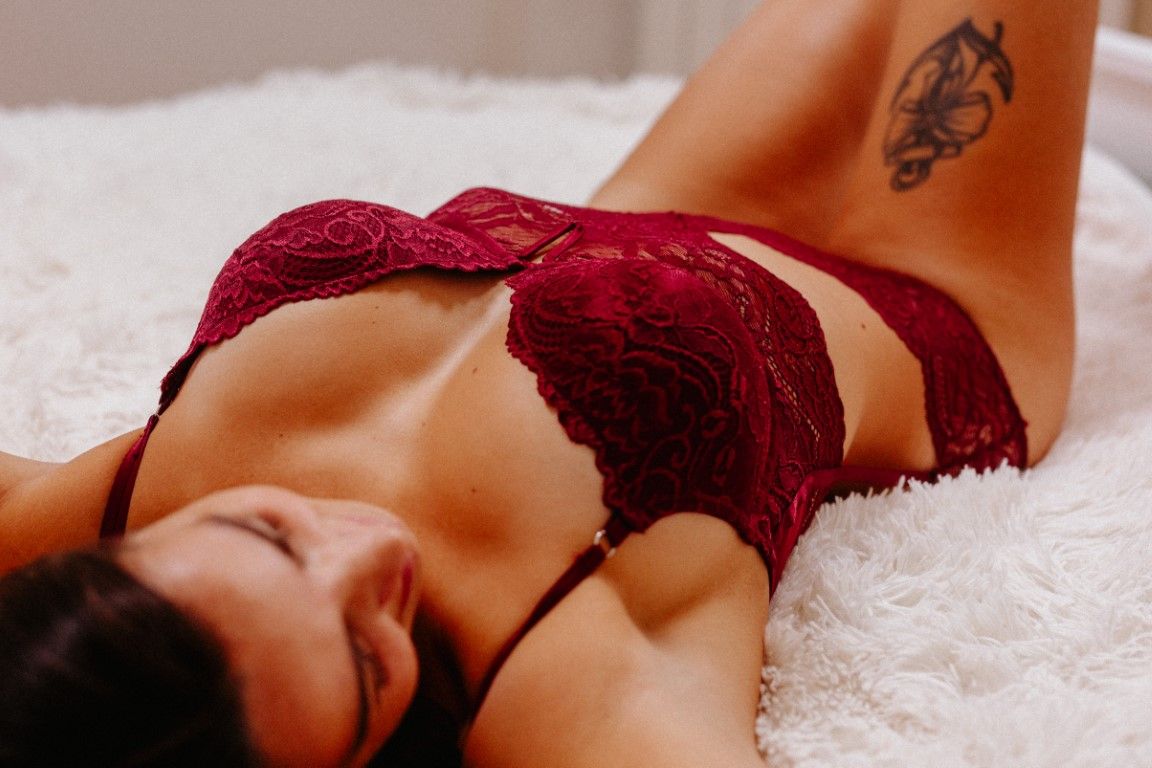 Woman lying on white fur, wearing red lace lingerie set with a tattoo visible on her side.