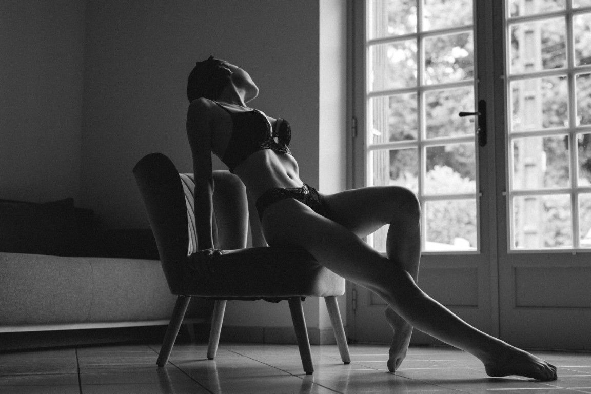 Artistic black and white silhouette of a woman sitting in a chair by large French windows.