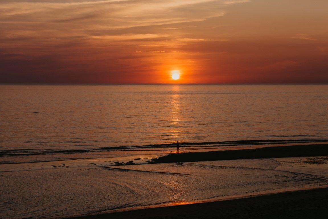 Un coucher de soleil à couper le souffle, aux teintes orangées et rouges, sur les eaux calmes de l'océan, avec une silhouette solitaire