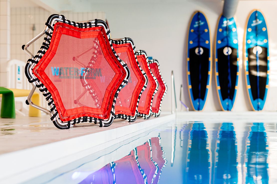 Red hexagonal water polo caps lined up beside an indoor swimming pool with surfboards.