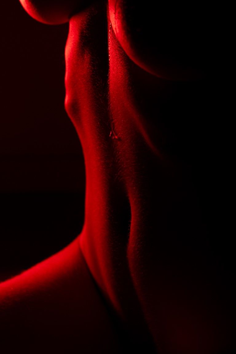 Close-up of a human neck and shoulder illuminated by dramatic red lighting against a dark background.