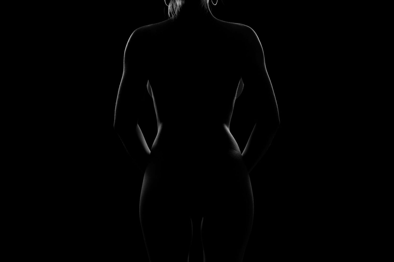 Silhouette of a woman's back against a dark background, highlighting her figure with dramatic low-key lighting.