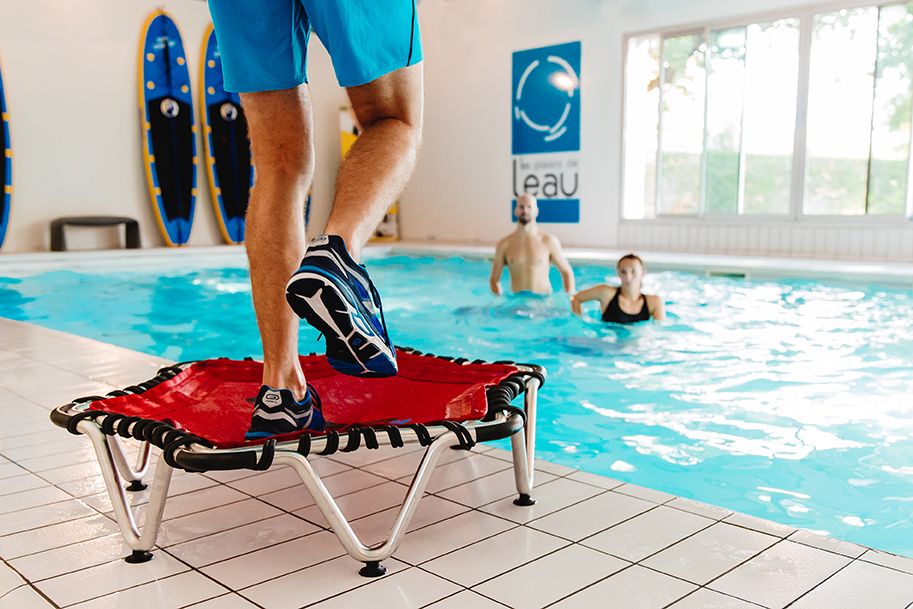 Instructor bouncing on a mini trampoline beside an indoor pool during aqua fitness class.