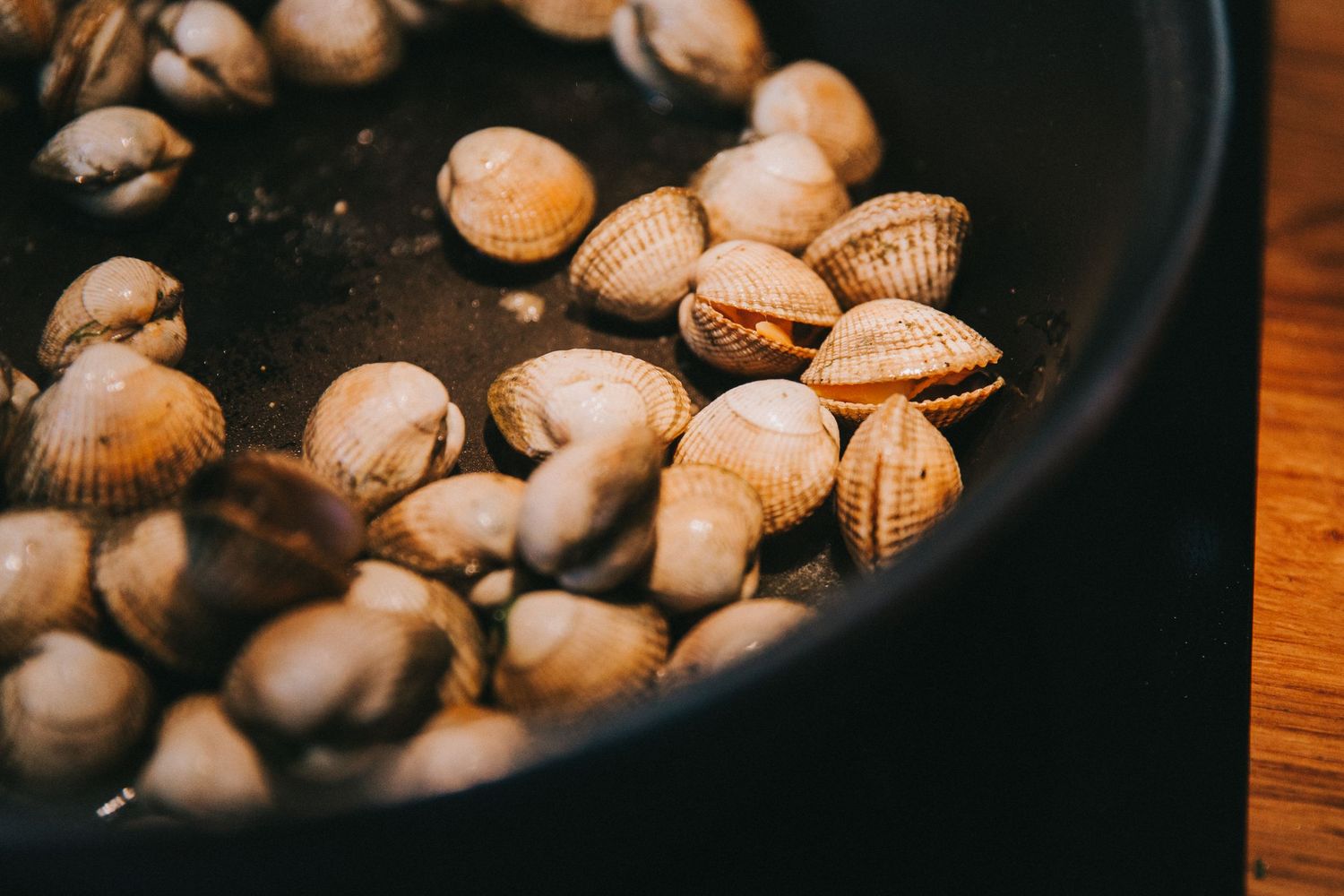 Fresh clams cooking in a dark cast iron pan on a wooden surface.