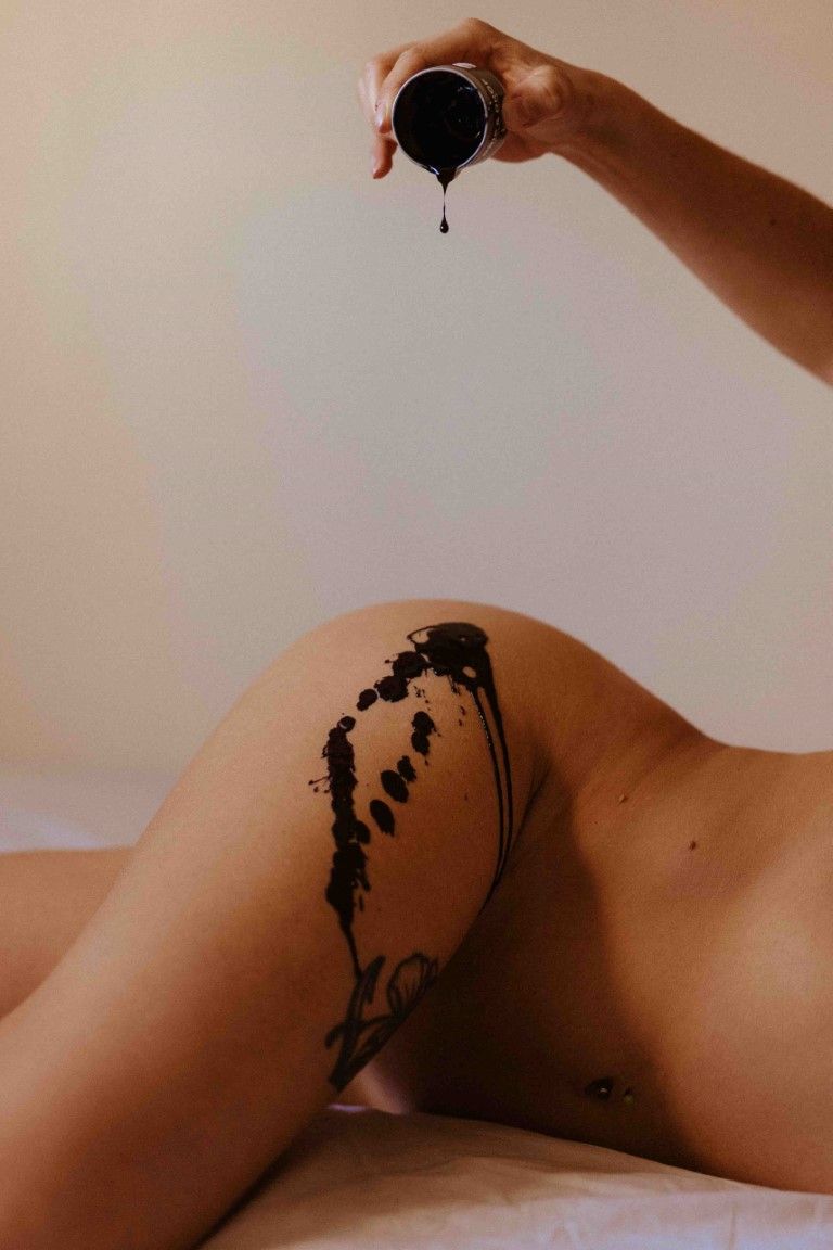 Artistic body photography with black liquid paint dripping onto bare skin creating abstract pattern.