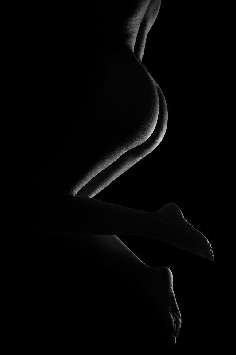 Black and white artistic silhouette photograph of a female figure seated against a dark background.