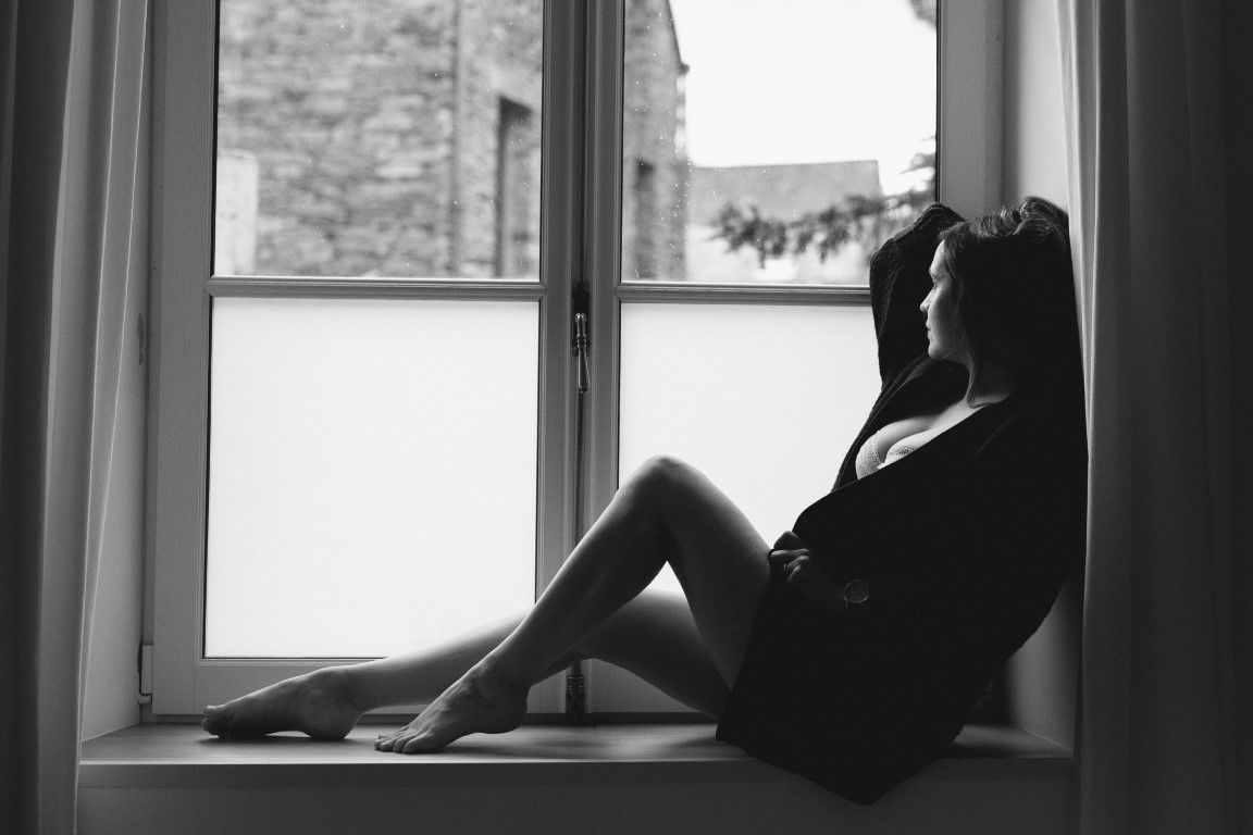 Black and white silhouette of a woman sitting on a windowsill gazing outside.