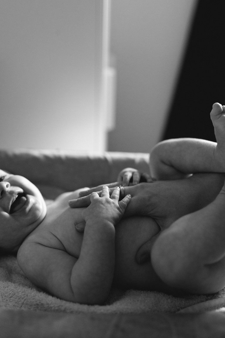Photo en noire et blanc de la main de la maman posée sur le ventre de sa petite fille qui rigole lors du changement de couche à St Lô.