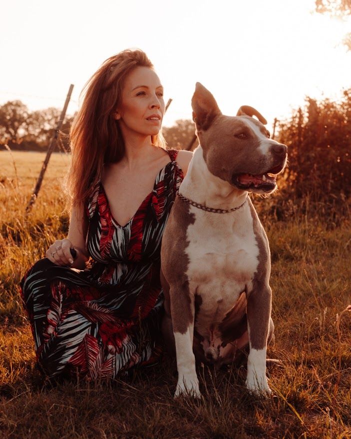 Femme en robe à fleurs assise à côté d'un pitbull brun et blanc au coucher du soleil.