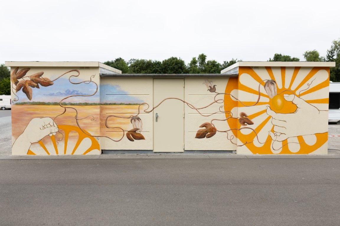 Colorful outdoor mural on a utility box featuring sun, leaves, and nature-inspired designs in orange, yellow, and blue tones.