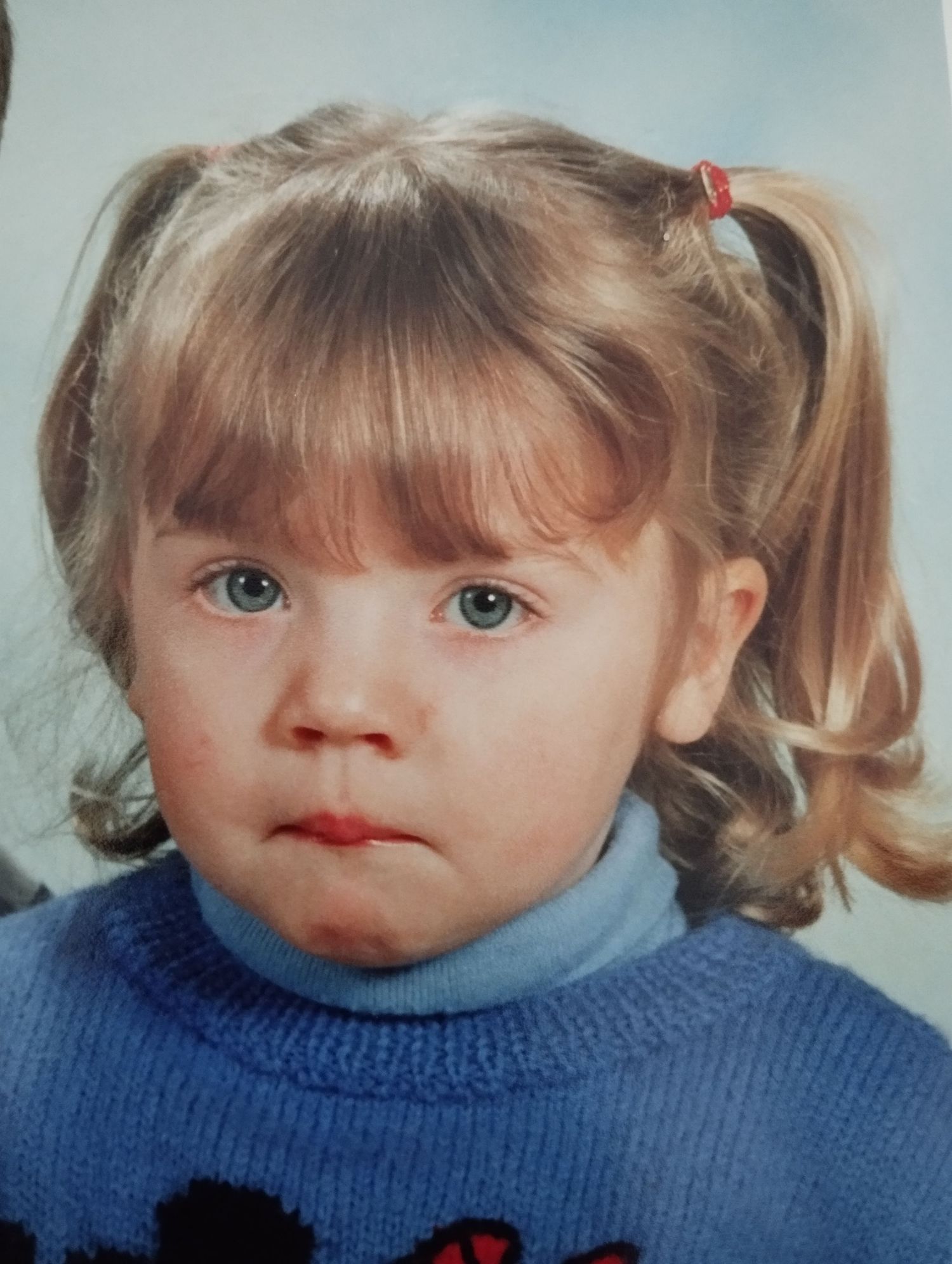 Jeune fillette en bas âge avec des couettes blondes et des yeux bleus portant un pull à col roulé bleu sur une photo de portrait.