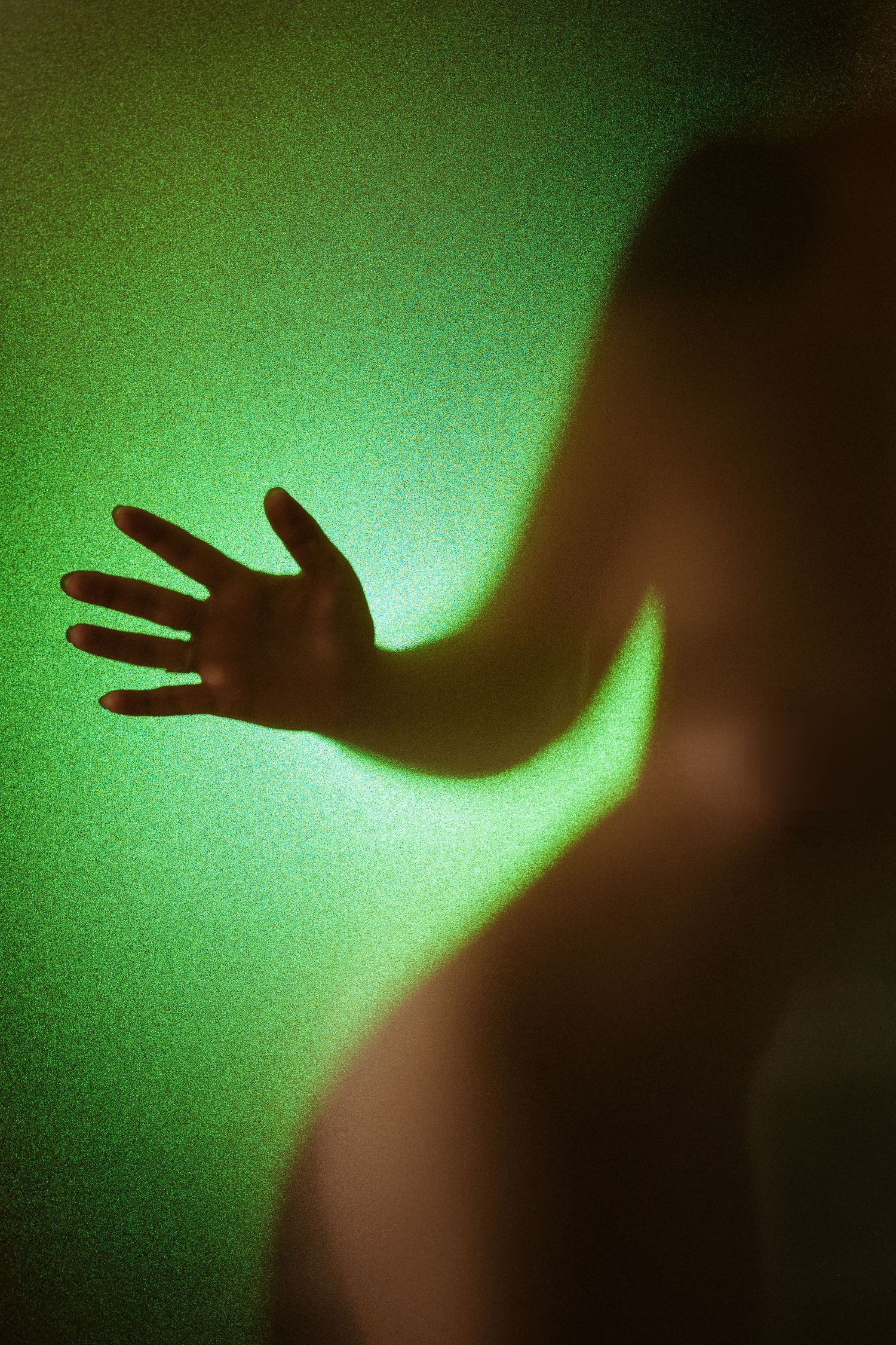 Silhouette of a hand pressed against frosted glass with eerie green lighting creating a mysterious, haunting effect.