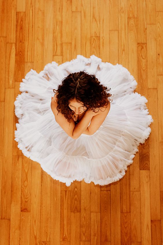 Vue aérienne d'une ballerine en tutu blanc assise gracieusement sur un parquet.