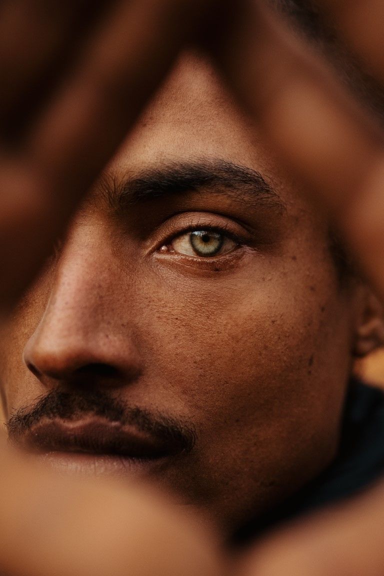 Portrait rapproché et intense d'un homme aux yeux verts, encadré par des mains floues.